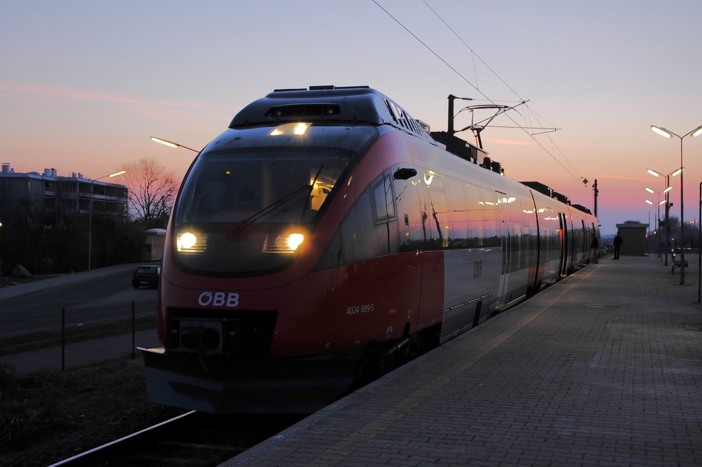 Trem vermelho entrando na estação, ao cair da noite